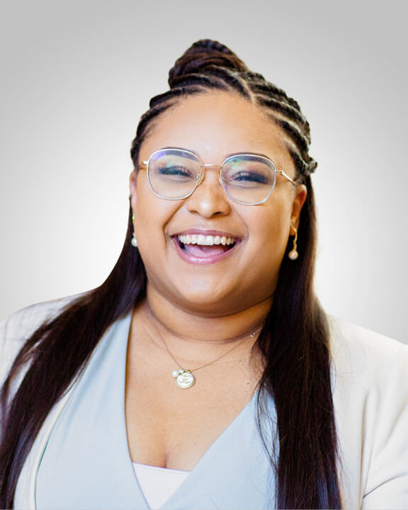 A portrait of a smiling person in a pale blue shirt and glasses with a light gray background