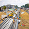 A major highway under construction with yellow cranes and trucks and personnel in orange safety gear