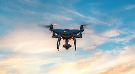 A black drone with red lights flying through a blue, cloudy sky