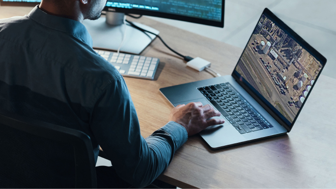 A person using a laptop at a desk viewing a video of a facility and parking lot