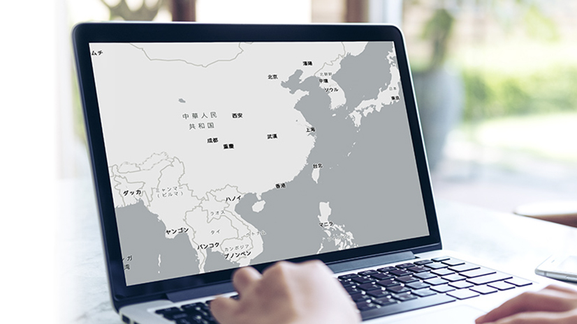 A pair of hands belonging to an unseen person typing on a laptop displaying a grayscale country map