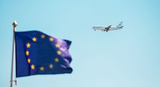 An airplane in the sky flying over a blue flag 