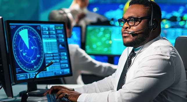 A person with headphones sitting in front of a computer monitor that is displaying air traffic on a radar