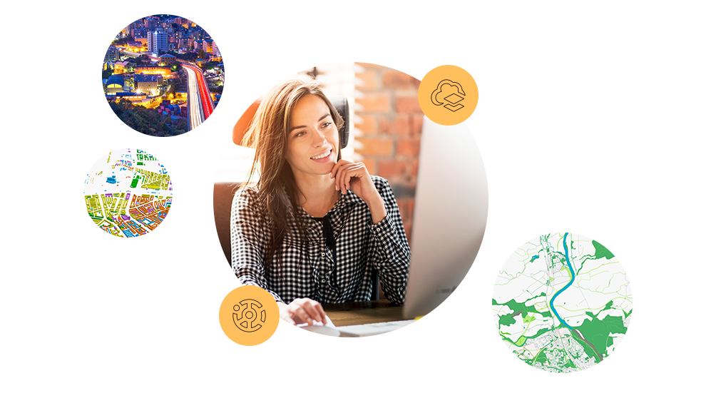 A woman at a desk smiling and working on a desktop computer next to two small images of a map and a city highway at night