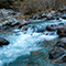 A full and quickly flowing creek surrounded by rocks and bushes