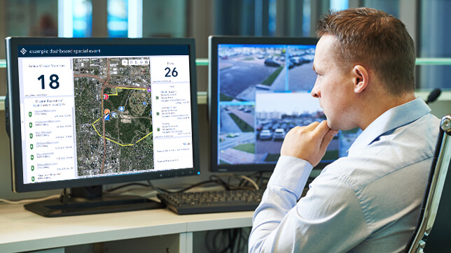 Man sitting at a desk with two computer monitors that show a 2D map and live video feeds with numerical data and text