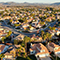 An aerial image of a sprawling residential development with pink-roofed white houses, clean curving streets, and many palm trees.