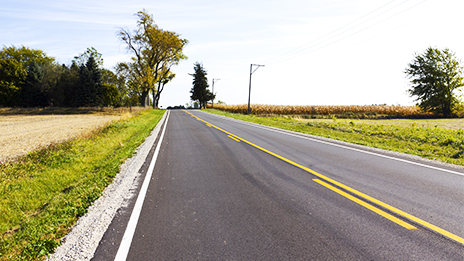 A two-lane road with green fields on both sides