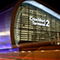 A sleek modern airport terminal with smoothly curving walls brightly lit in white, gold, and blue under a black night sky