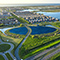 An aerial view of a neighborhood near the water and a circular plot of land with rows of solar panels