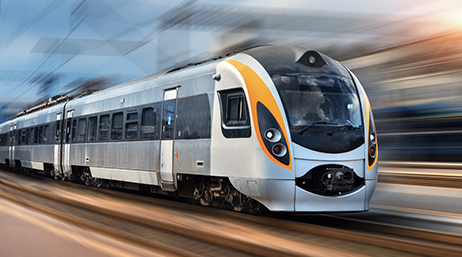 A modern steel bullet train running down an outdoor track with surrounding scenery and sky blurred to convey great speed