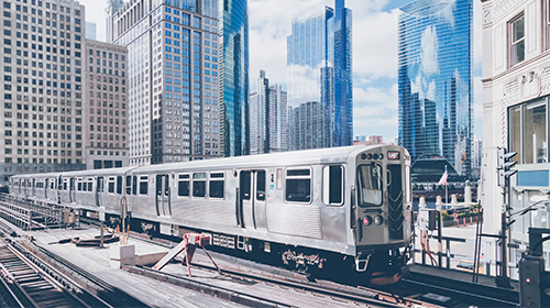 Two elevated L train tracks with two rail cars surrounded by modern, high-rise buildings in downtown Chicago