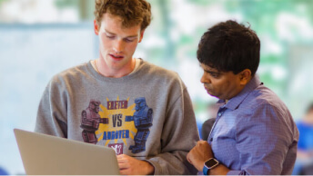 Two casually dressed people discussing a laptop display held in their hands in a sunlit modern office space