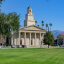 A historic tree-filled university campus with wide green fields under a vivid clear blue sky