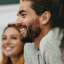 A closeup of two smiling people gazing into the distance with a soft-focus white background