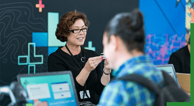 A photo of a conference staffer helping a registrant, while a person in a backpack stands in the foreground,A photo of a conference staffer helping a registrant, while a person in a backpack stands in the foreground