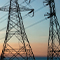 A row of utility poles strung with wires stretching into the distance silhouetted against a pale blue and orange sunset sky