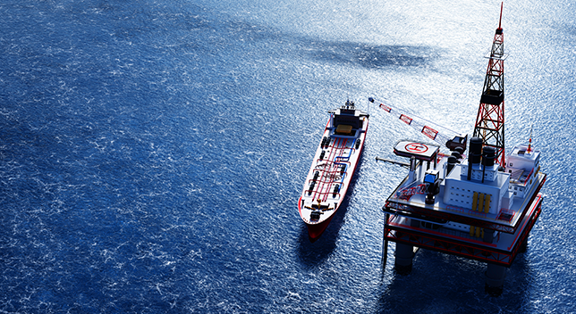 An aerial photo of a ship beside an oil rig surrounded by a large expanse of sparkling calm blue sea