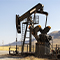 A photo of a pumpjack in a pale yellow desert with a pale blue sky overhead