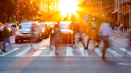 Blurry figures of people walking on a crosswalk in front of stopped cars