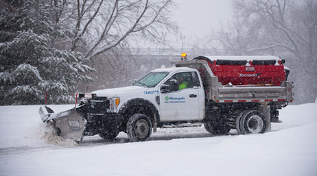 A snowplow clearing a road while it snows 