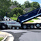 A crew in yellow vests and white hard hats working with a blue and white truck with attached pavement repair equipment on a tidy tree-lined residential street