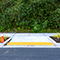 An access ramp set joining a paved road and a sidewalk lined with tall green hedges