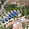 An aerial image of a large modern complex with neat green landscaping, a pink tile roof and rows of solar panels alongside a wide tree-lined road