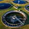 An aerial photo of a water purification site surrounded by sunny green fields and a nearby highway