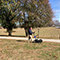 A person pushing a land survey data collection device across a grass field