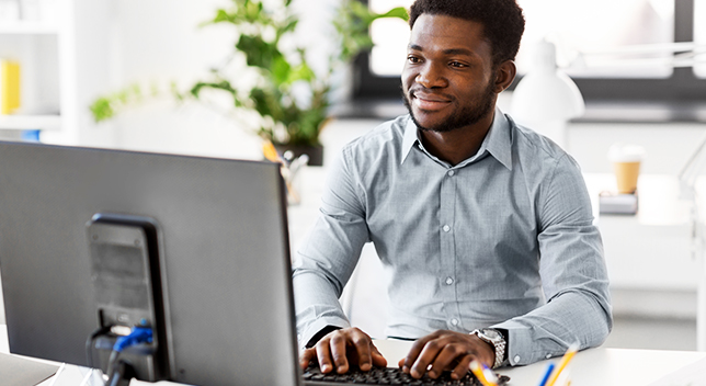 A person sitting at a desk typing on a desktop computer