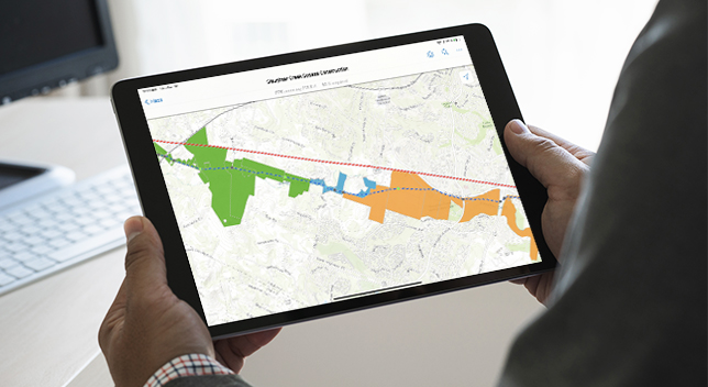 A person holding a tablet displaying a map with an orange, blue, and green highlighted area