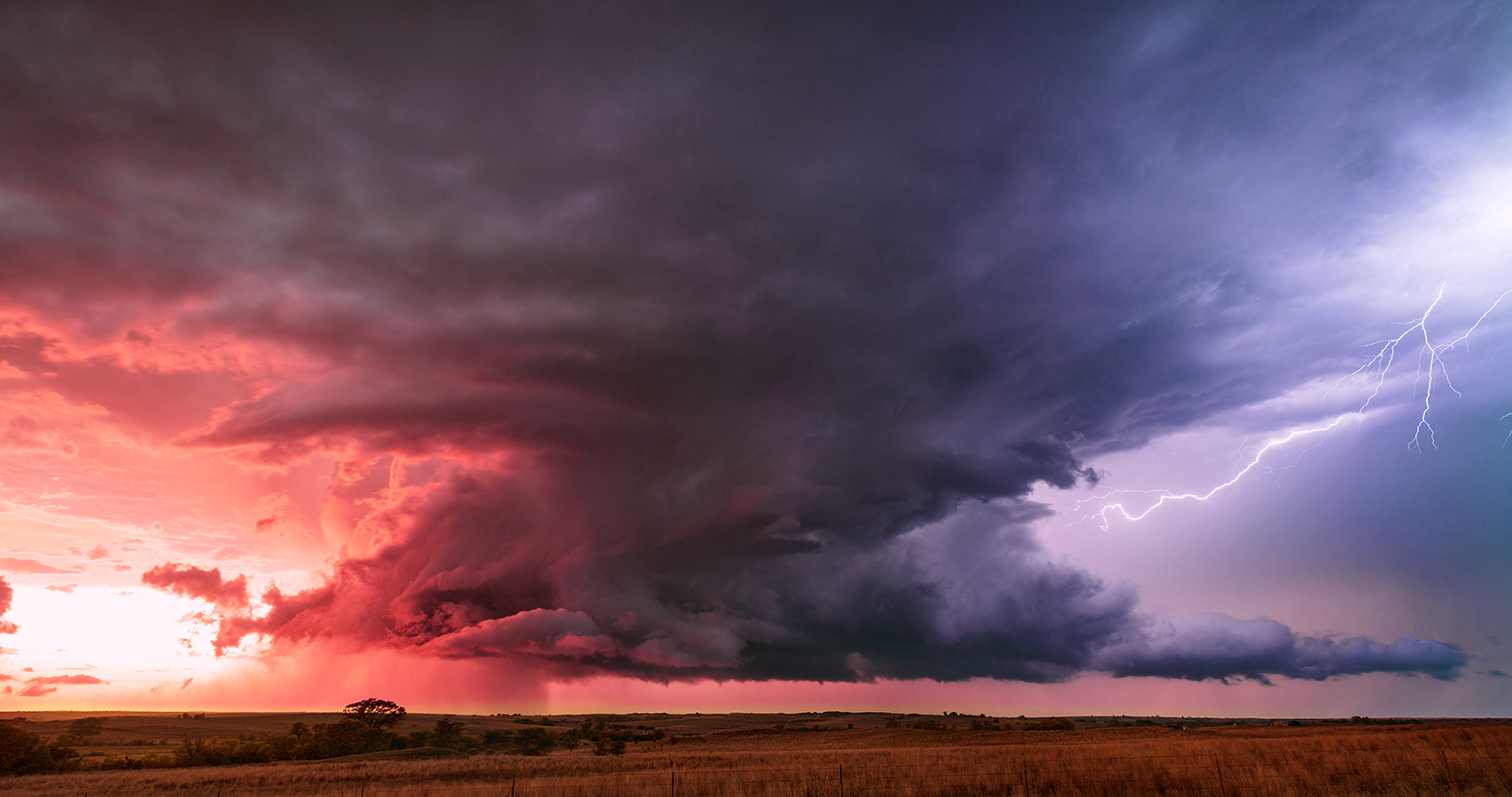 A pink and purple sunset shining on the clouds and across a plain